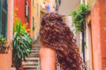 The back of a woman's head as she turns into a rustic alleyway.